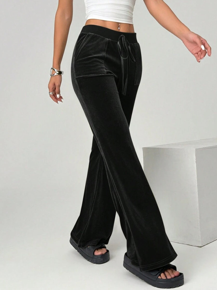 Black velvet pants worn by a person on a plain background