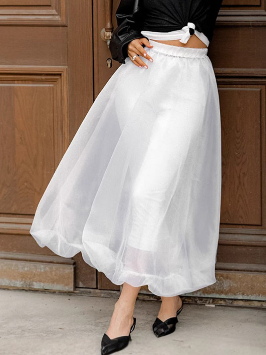 Person wearing a white skirt and black top in front of a wooden door.