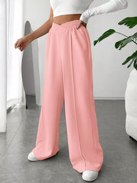 Person wearing pink wide-leg pants and a white top in a minimal indoor setting.
