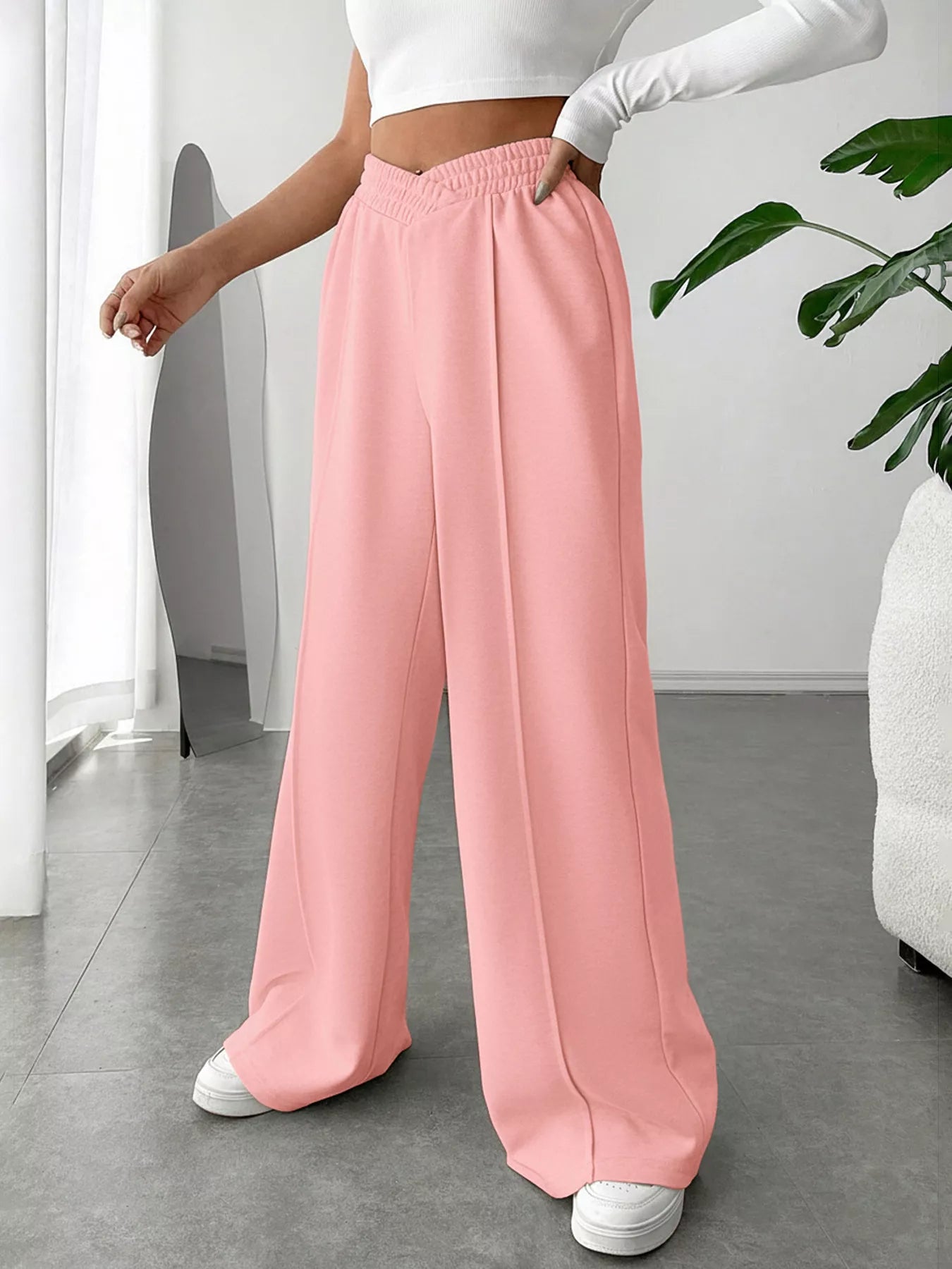 Person wearing pink wide-leg pants and a white top in a minimal indoor setting.