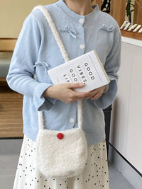 Person holding a white textured bag with a red button and a book titled 'Good Vibes Good Life'.
