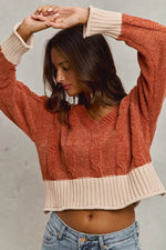 Woman wearing a rust-colored sweater with beige trim against a neutral background
