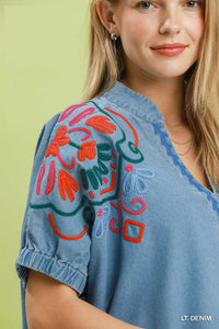 Woman wearing a light blue denim shirt with colorful embroidery on a green background