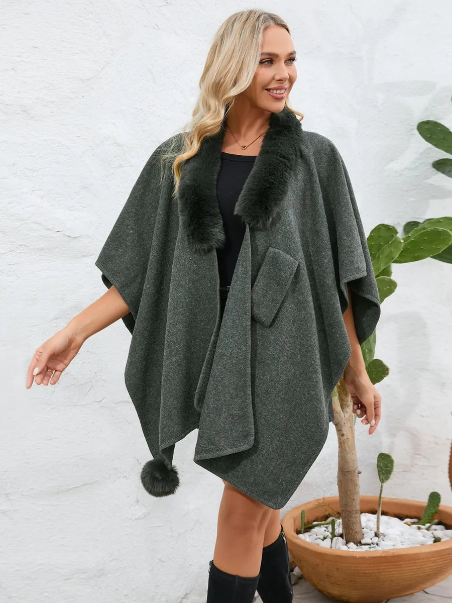 Woman wearing a gray poncho with fur trim in front of a white wall.