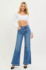 Woman wearing a white long-sleeve top and blue flared jeans on a white background