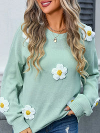 Green sweater with white daisy flower designs worn by a person.