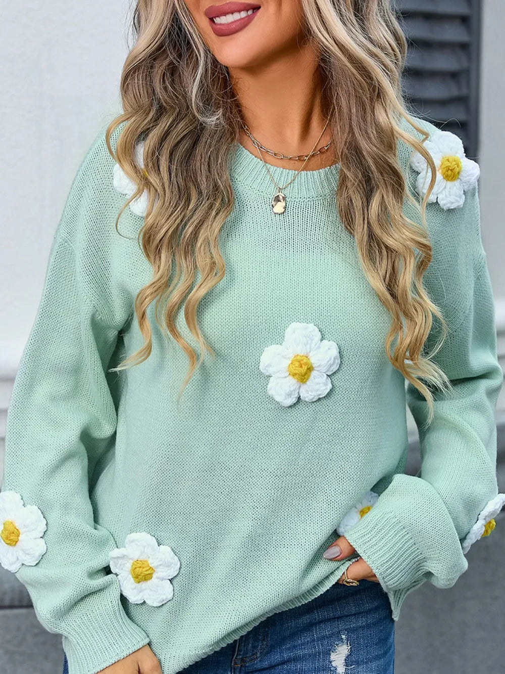Green sweater with white daisy flower designs worn by a person.
