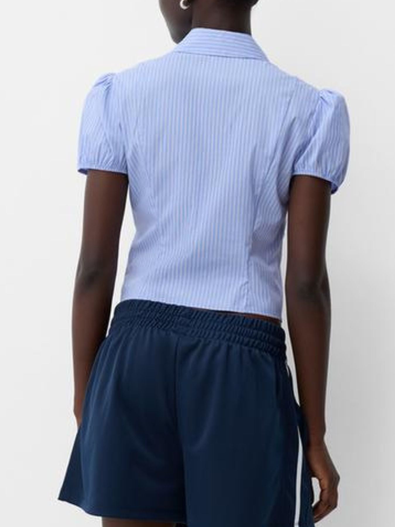 Person wearing a light blue striped shirt and navy shorts on a white background