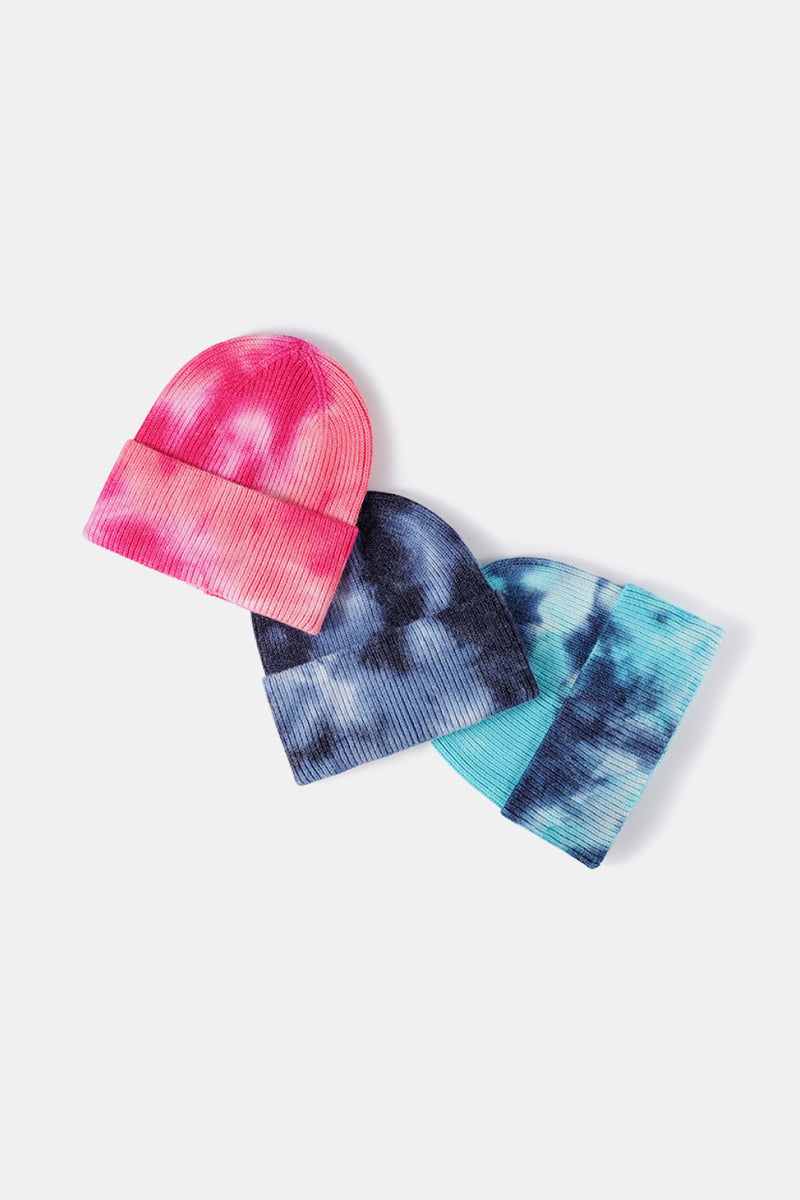Three tie-dye beanies in pink, blue, and black on a white background