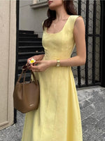 Woman in a yellow dress holding a brown handbag, standing on a street.