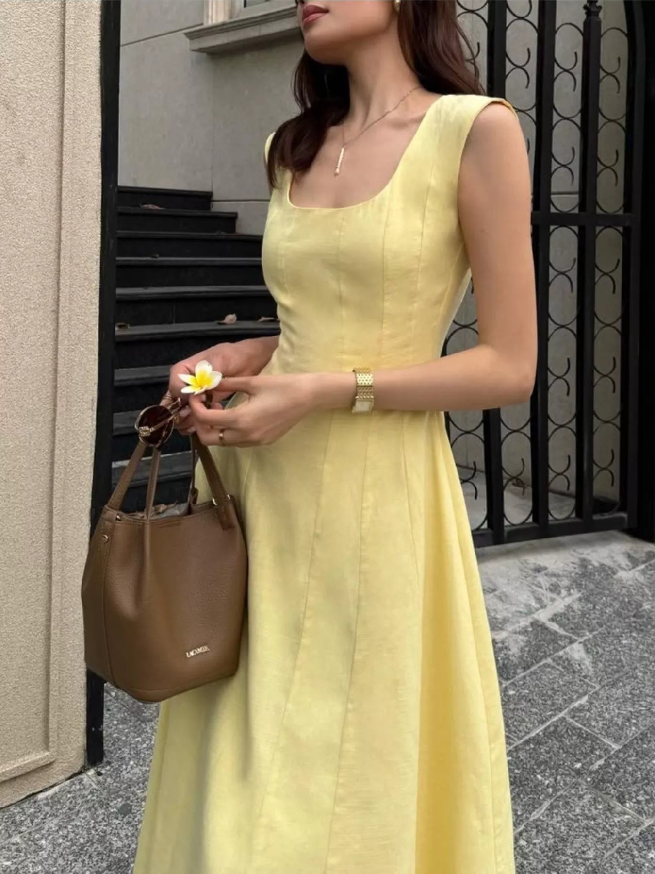 Woman in a yellow dress holding a brown handbag, standing on a street.