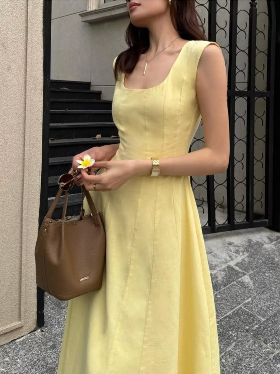 Woman in a yellow dress holding a brown handbag, standing on a street.