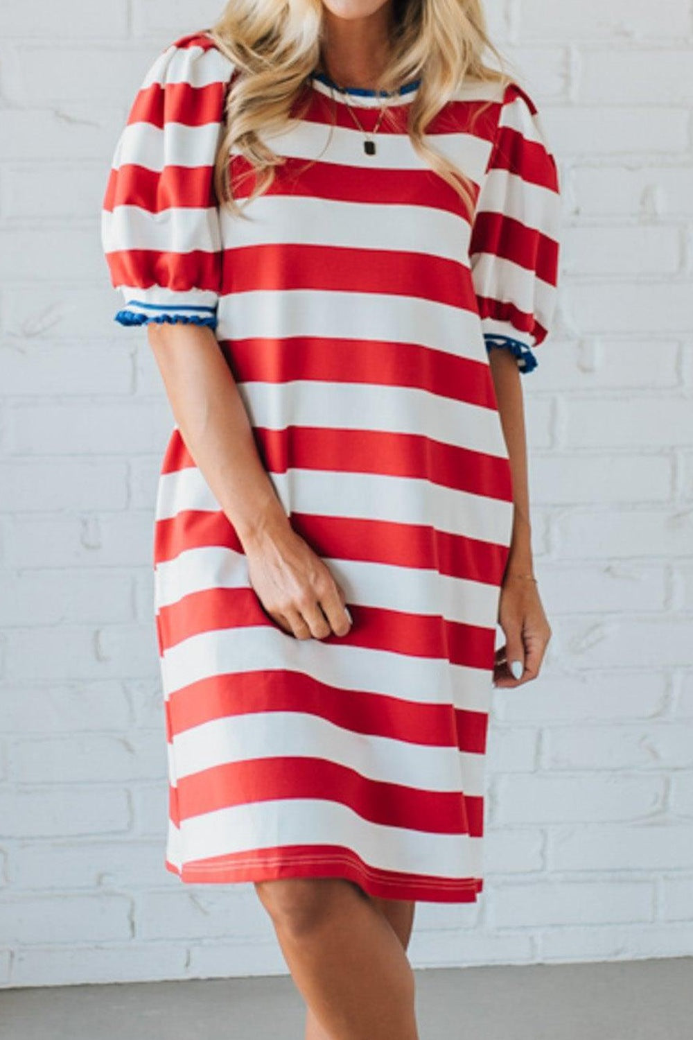 Red and white striped dress worn by a person against a white brick wall.