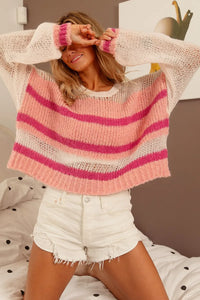 Woman wearing a pink and white striped sweater and white shorts, sitting on a bed.