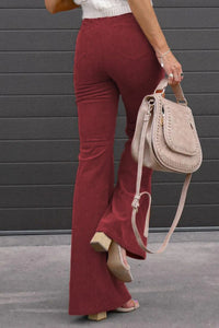 Person wearing red flared pants and holding a beige handbag against a gray background
