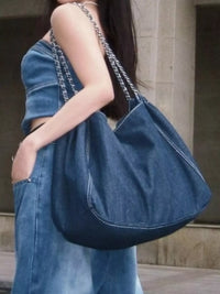 Person holding a denim handbag with a neutral background