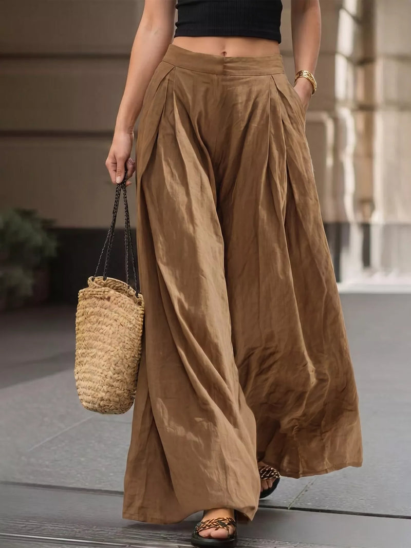 A person wearing high-waisted, wide-leg brown pants with a black crop top, carrying a woven straw tote bag, walking outdoors.