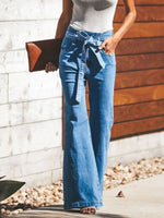 Person wearing blue jeans with a white top, standing against a wooden wall.