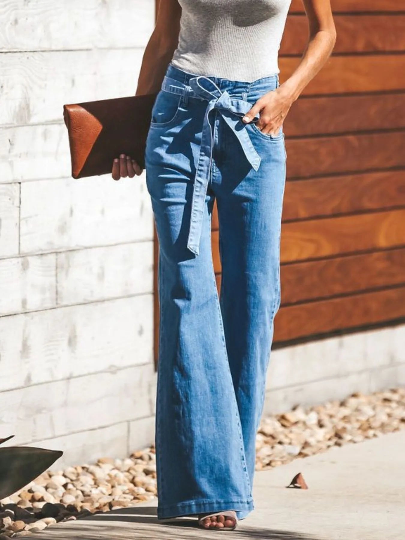 Person wearing blue jeans with a white top, standing against a wooden wall.
