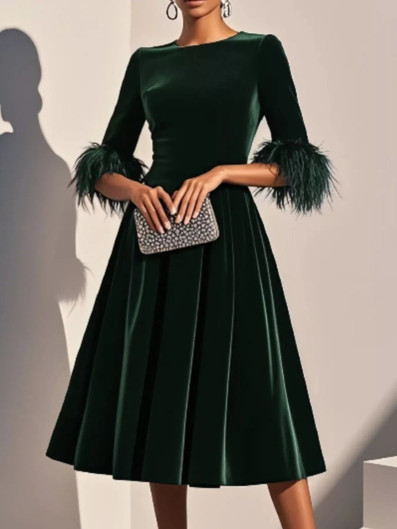 Green velvet dress with feathered sleeves held by a hand with a clutch against a neutral background