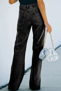 Person wearing high-waisted black jeans holding a silver handbag against a light background