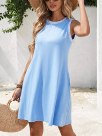 Woman wearing a light blue dress with a white wall and plant in the background