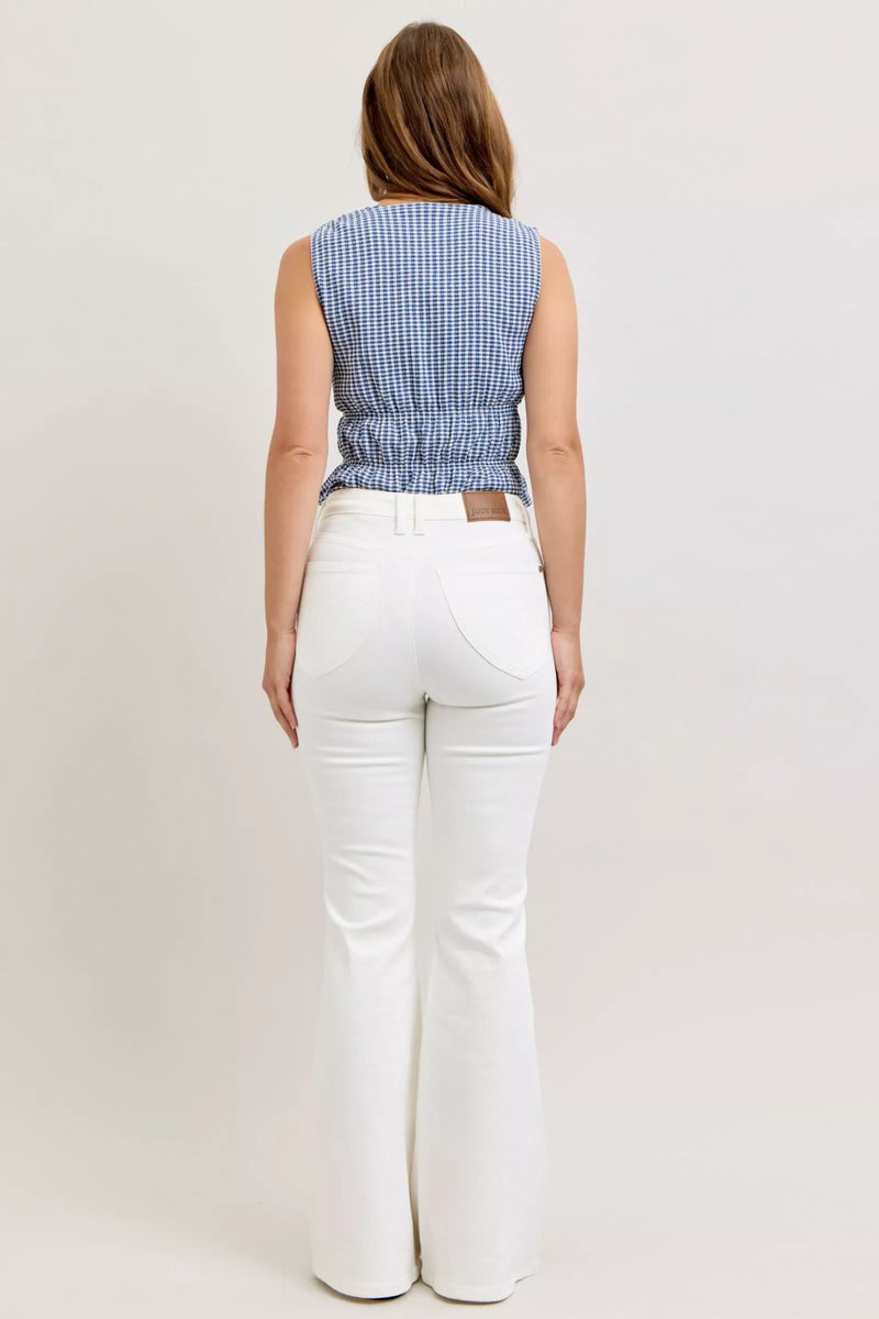 Woman wearing a blue checkered top and white pants on a plain background