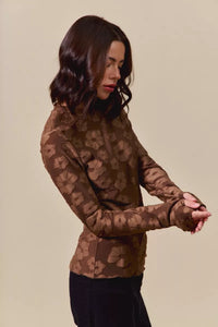 Woman wearing a brown patterned long-sleeve top against a beige background