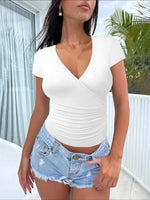 Woman wearing a white top and denim shorts on a balcony with plants in the background