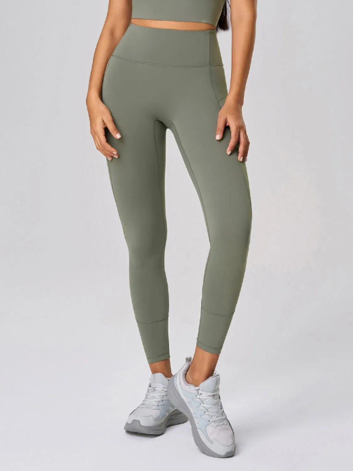 Person wearing olive green leggings and white sneakers on a light gray background