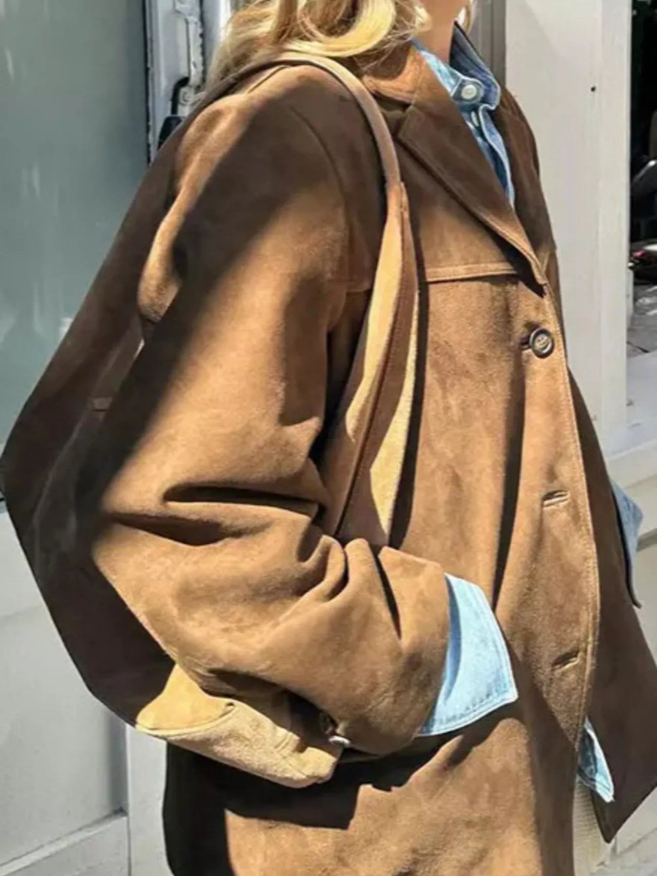 Person wearing a brown suede jacket with a light blue shirt underneath, standing against a neutral background.