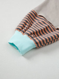 Folded fabric with brown and black horizontal stripes and a light blue edge on a light gray background