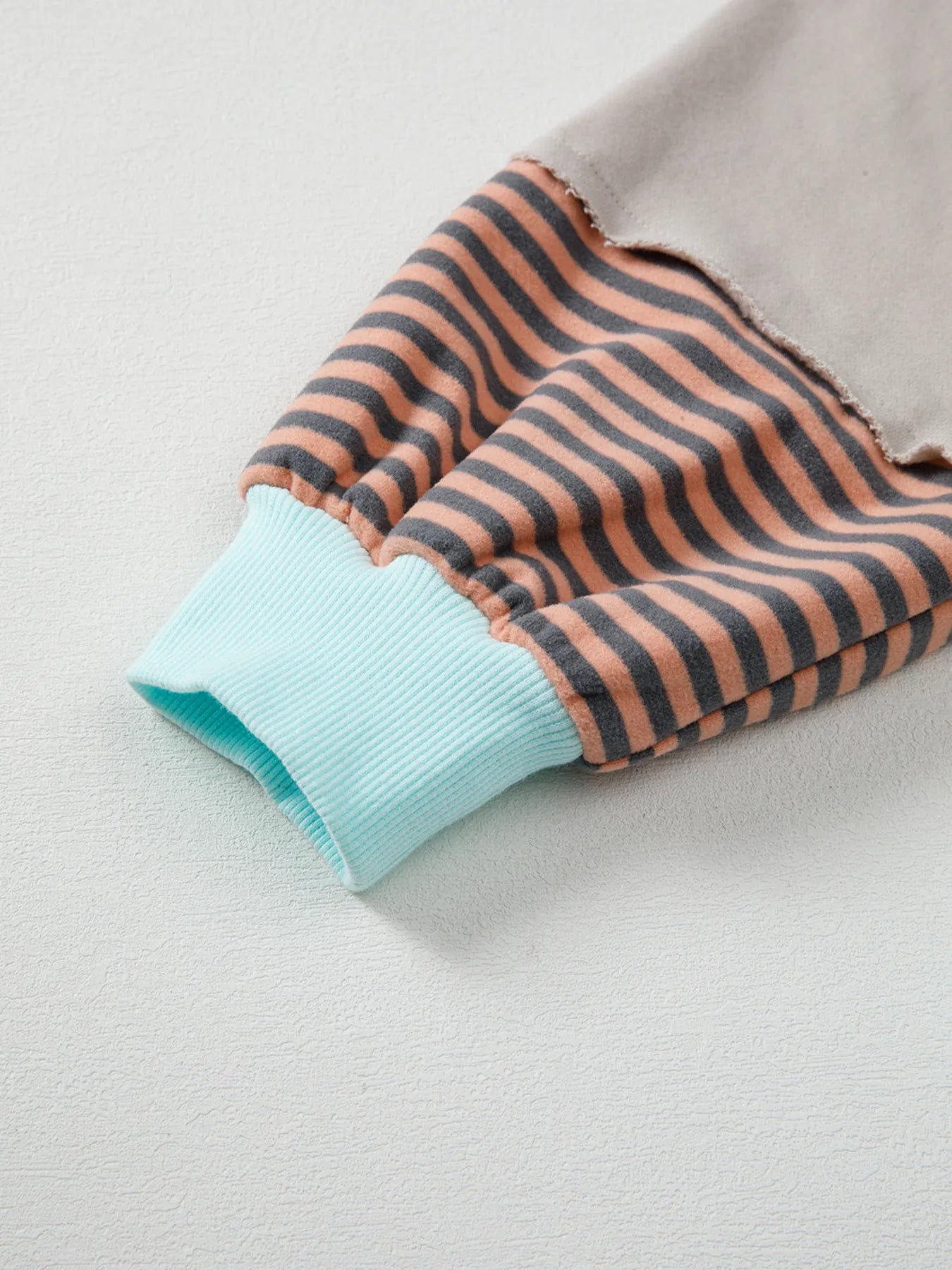 Folded fabric with brown and black horizontal stripes and a light blue edge on a light gray background