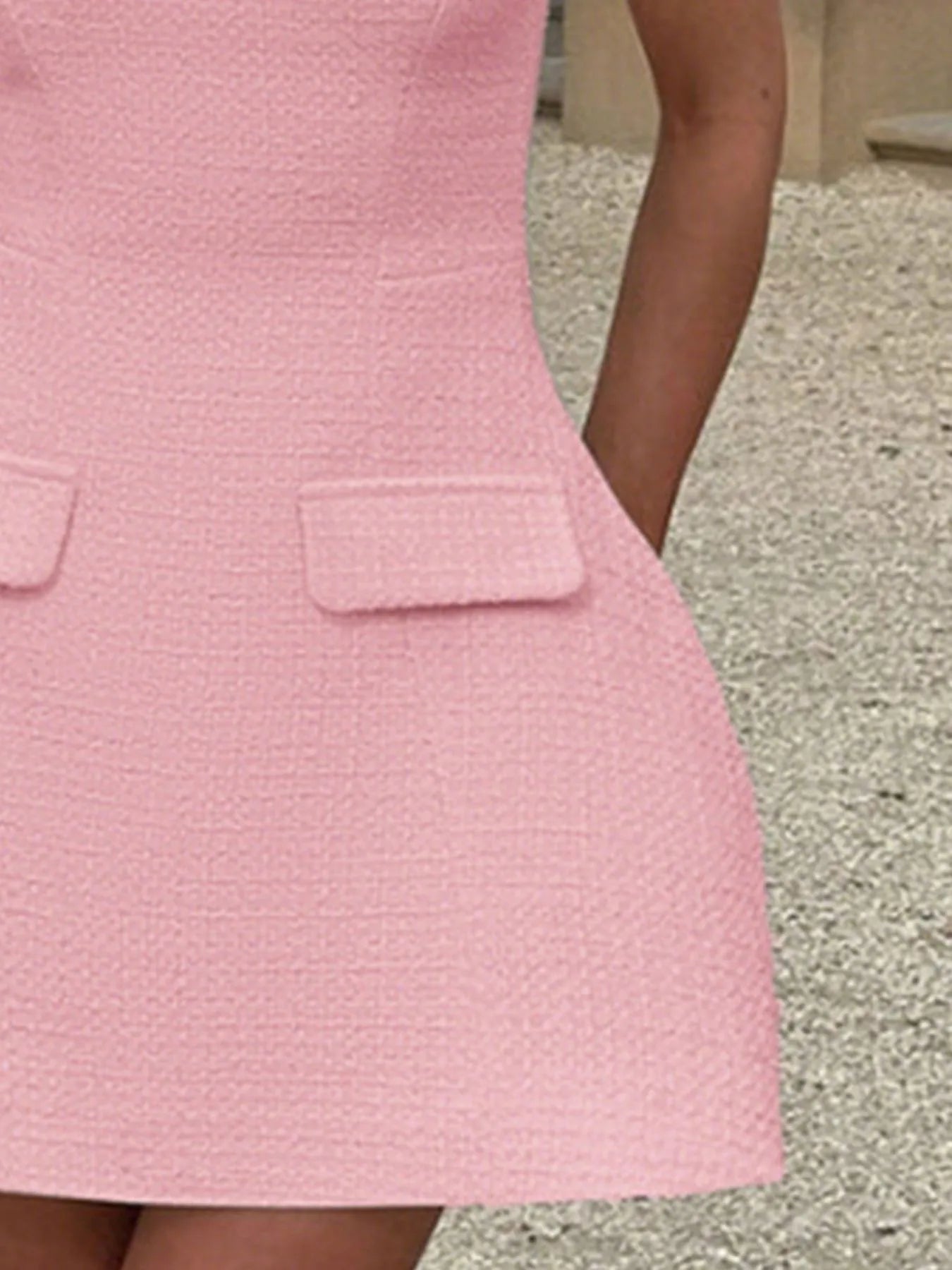 Close-up of a pink textured dress with two front pockets on a neutral background.
