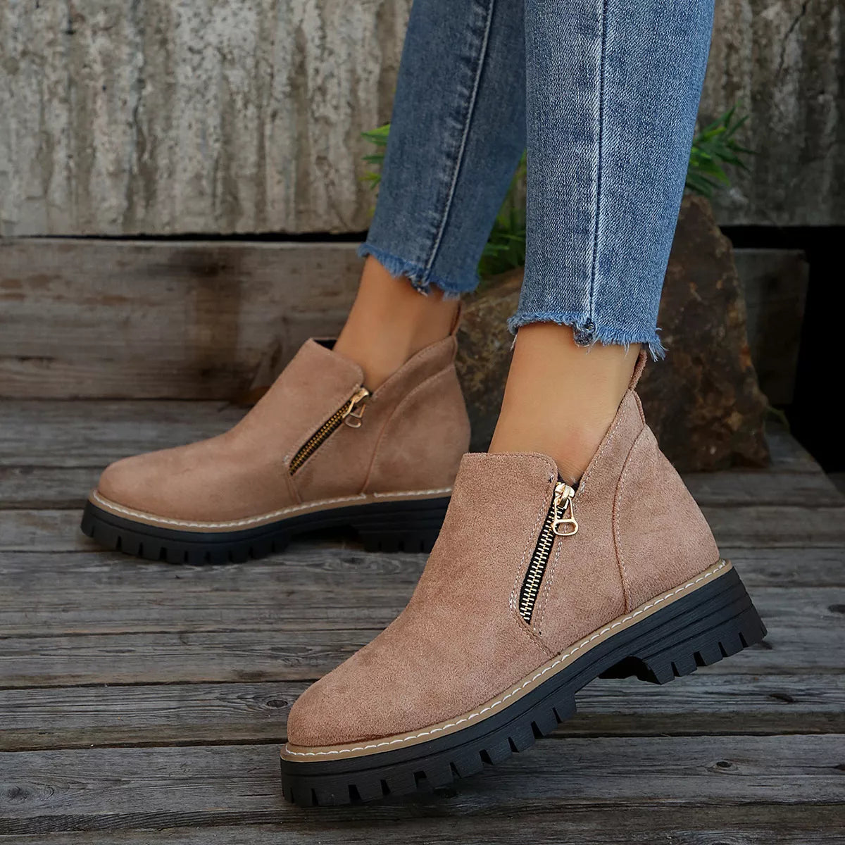 Tan ankle boots with zippers worn with blue jeans on a wooden floor.