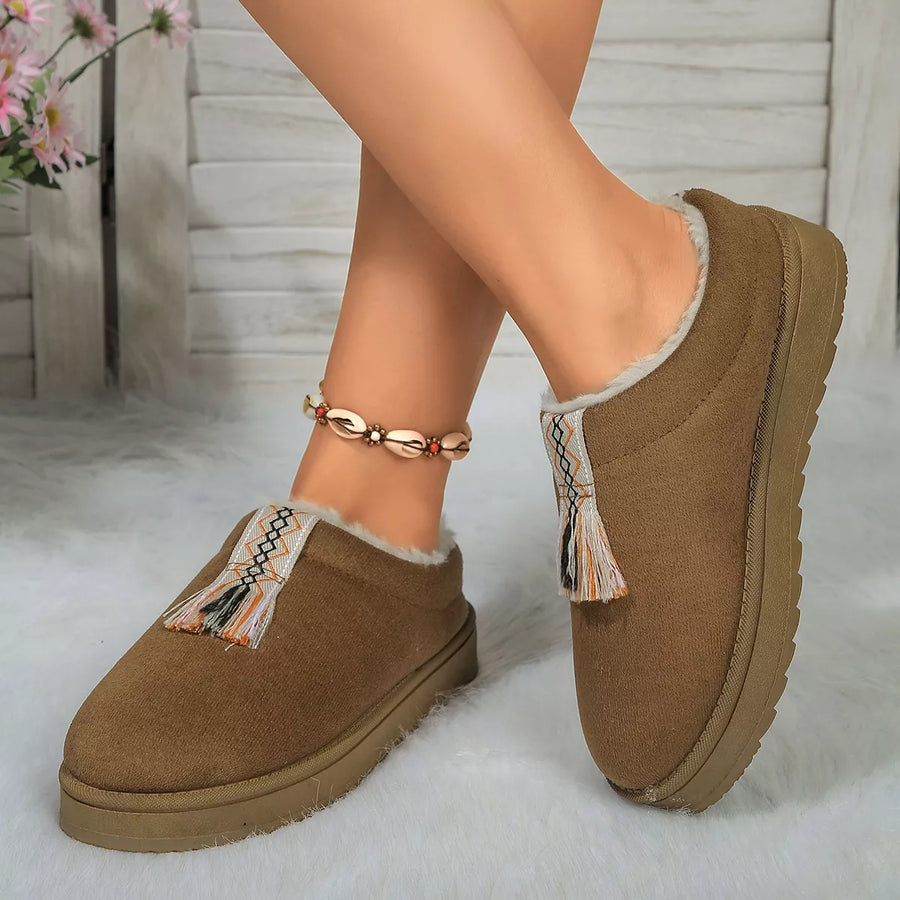 Brown slippers with decorative tassels worn by a person on a light background