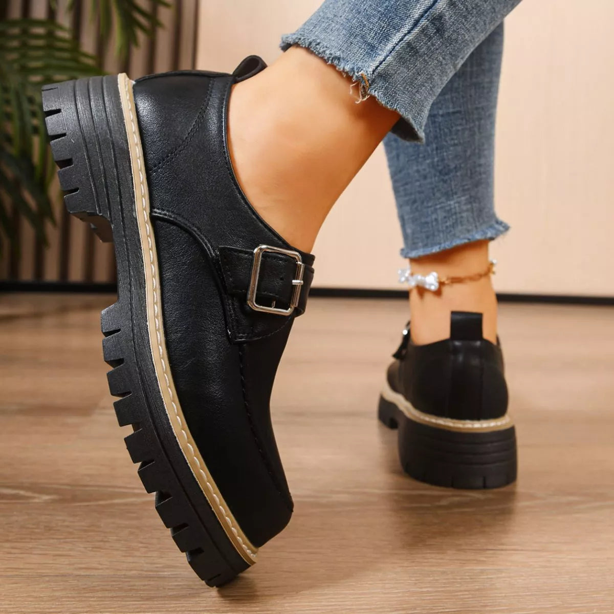 Black leather shoes with a buckle worn by a person on a wooden floor.