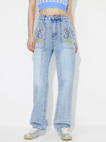 Person wearing light blue jeans with embroidered designs on a white background