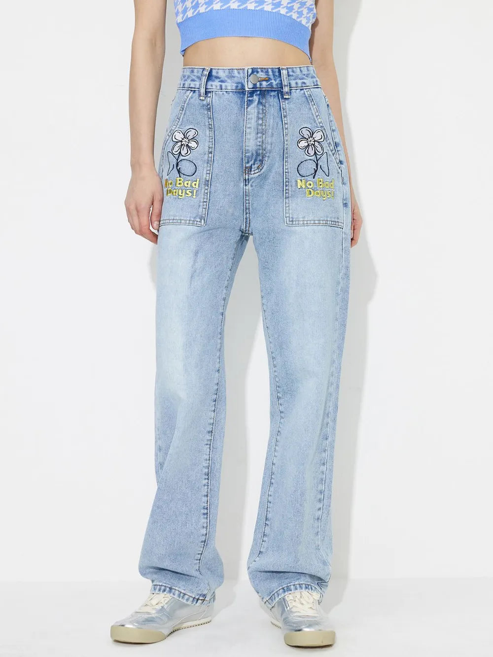 Person wearing light blue jeans with embroidered designs on a white background