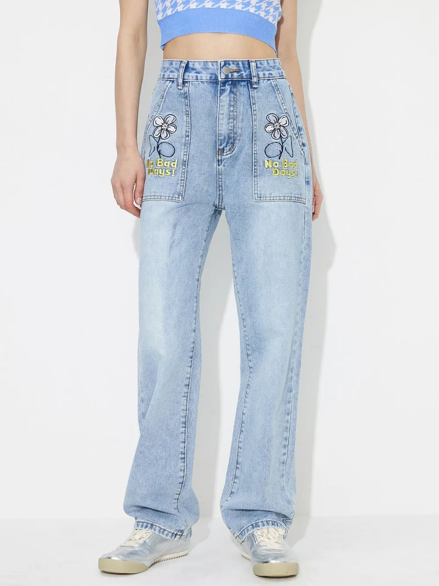 Person wearing light blue jeans with embroidered designs on a white background
