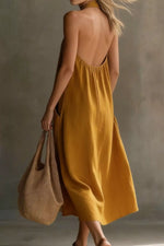 Woman wearing a mustard yellow dress holding a brown bag against a neutral background