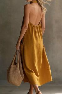 Woman wearing a mustard yellow dress holding a brown bag against a neutral background