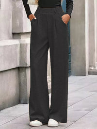Person wearing dark gray wide-leg pants standing against a stone wall.