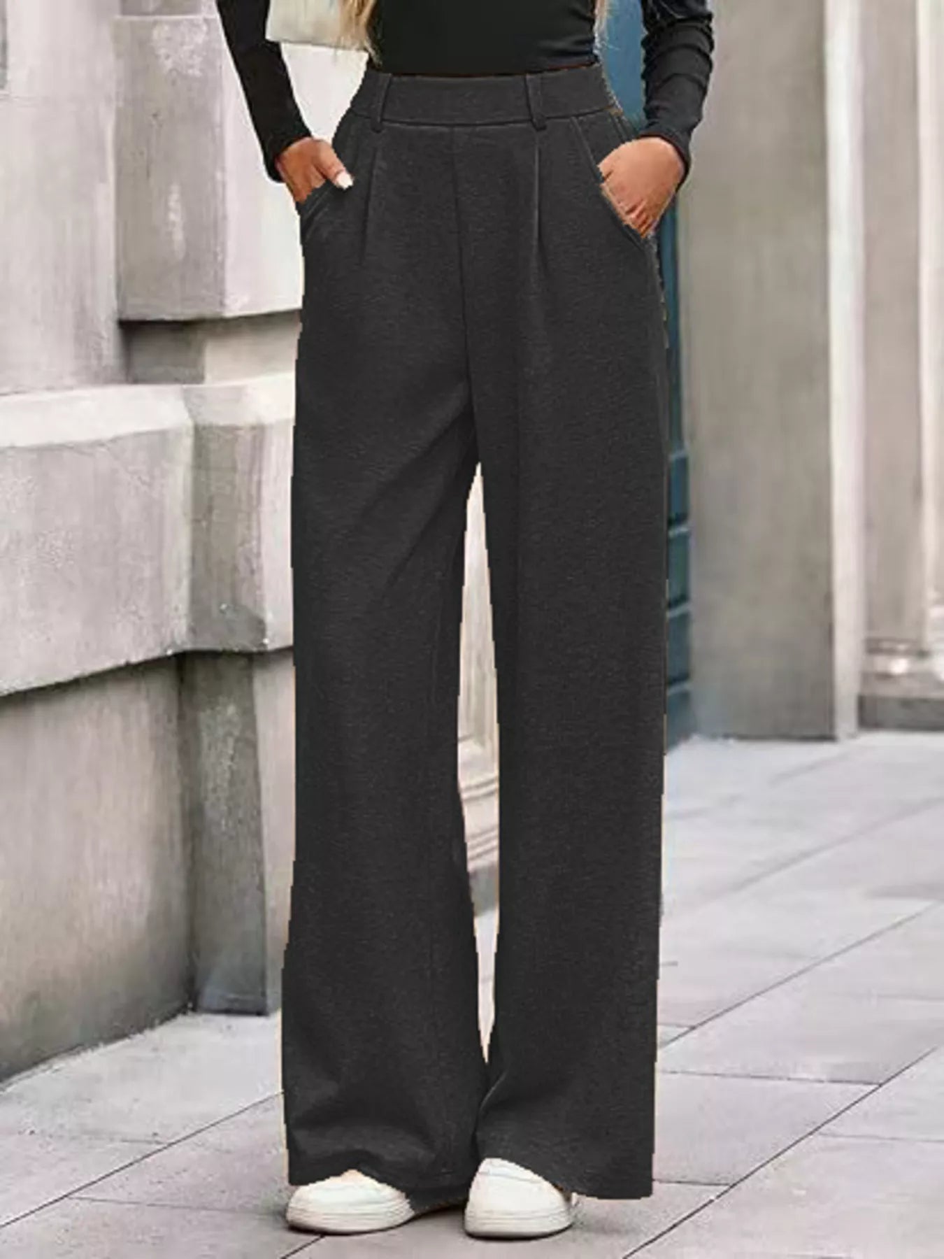 Person wearing dark gray wide-leg pants standing against a stone wall.