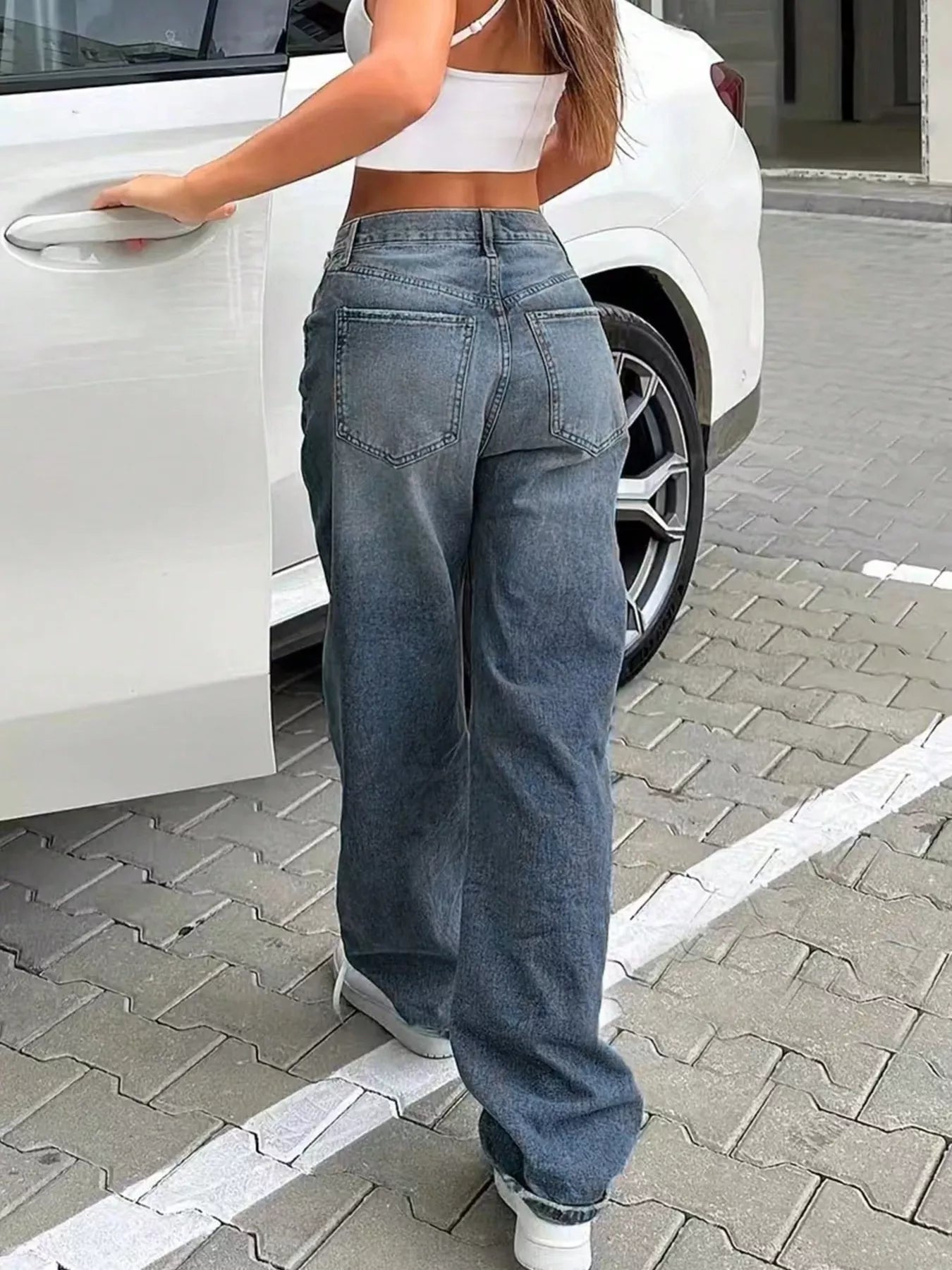 Person wearing blue jeans and a white crop top getting into a white car.