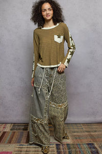 Woman wearing a long-sleeve top and wide-leg pants against a gray wall.