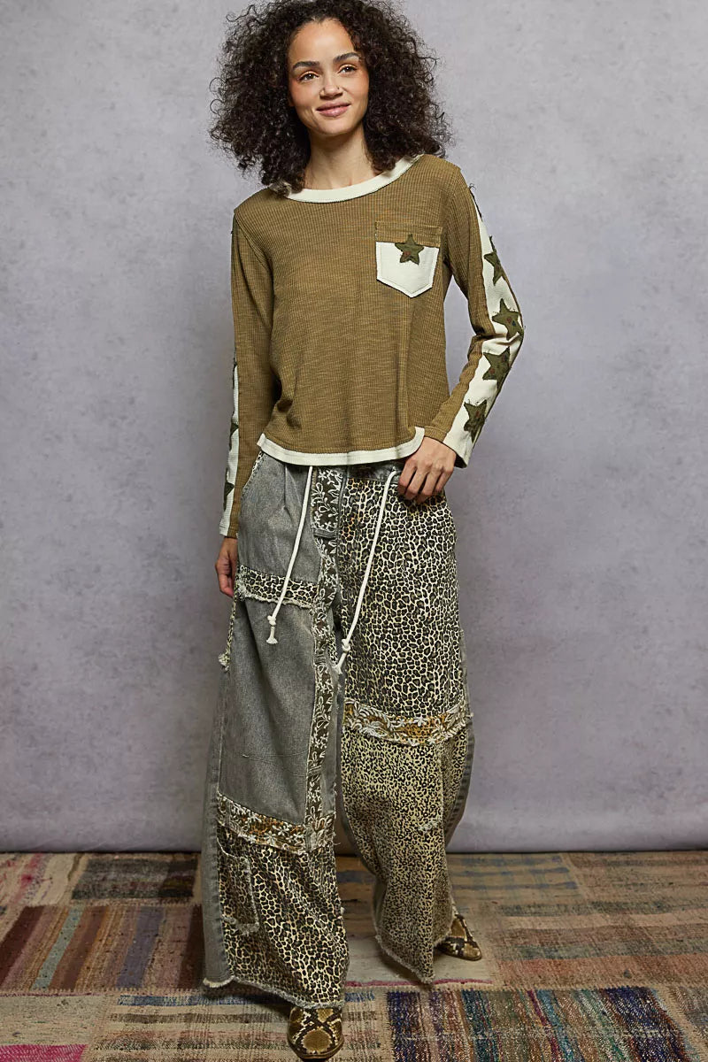 Woman wearing a long-sleeve top and wide-leg pants against a gray wall.