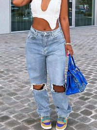 Person wearing ripped jeans and a white crop top, holding a blue bag on a street.
