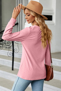 Woman wearing a pink sweater and tan hat, standing on a sidewalk.