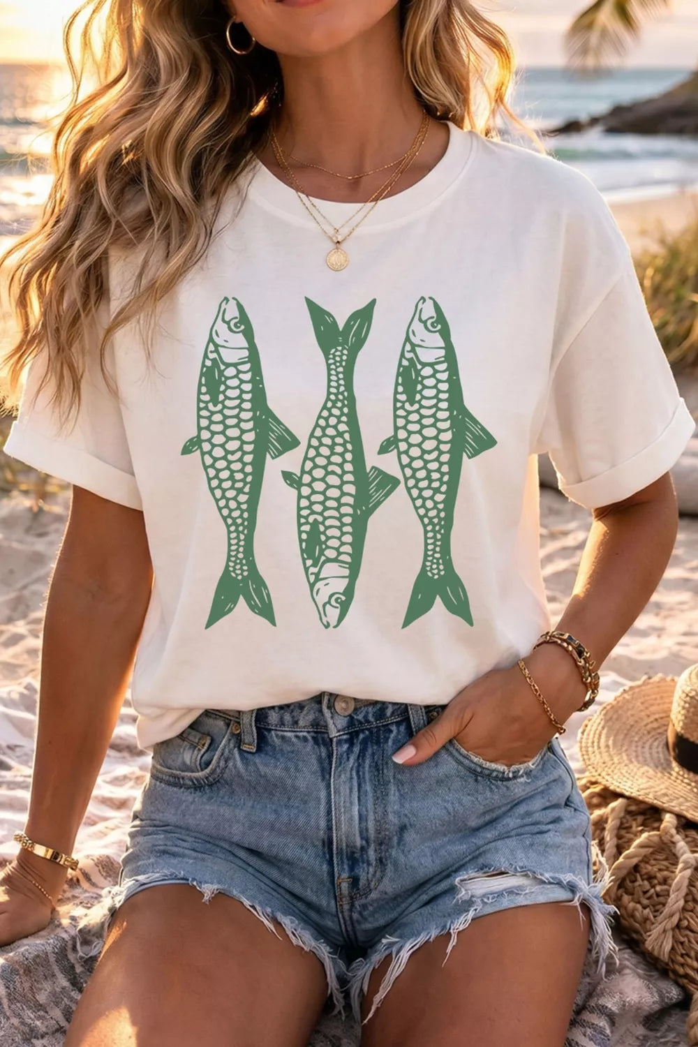 Person wearing a white t-shirt with green fish graphics on a beach.